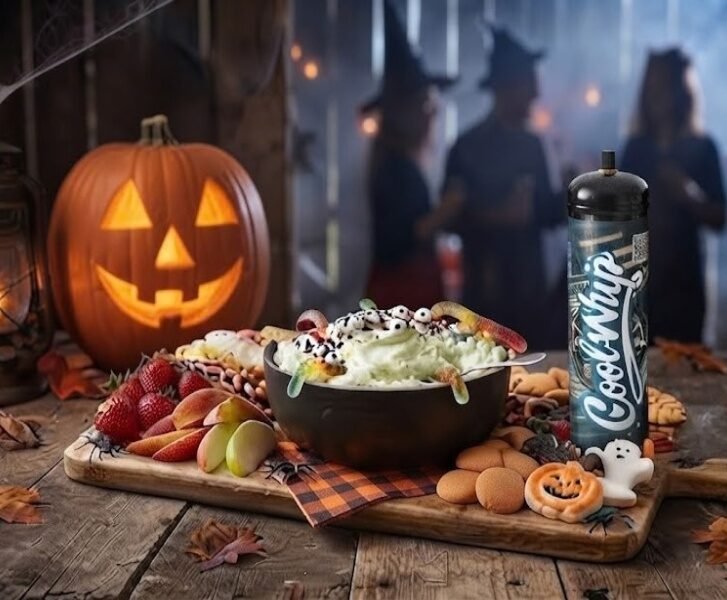 Cool Whip Cream Halloween dip board with a black bowl of green dip topped with candy eyeballs and gummy worms beside fruit and cookies